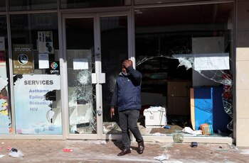 El propietario de una tienda saqueada camina por el escaparate roto en el marco de las protestas tras el encarcelamiento del ex presidente de Sudáfrica Jacob Zuma, en Katlehong, el 12 de julio de 2021 (REUTERS/Siphiwe Sibeko)