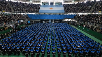 Estadio interior con miles de policías uniformados saludando en filas, una gran bandera de Argentina, gradas llenas de público y un escenario