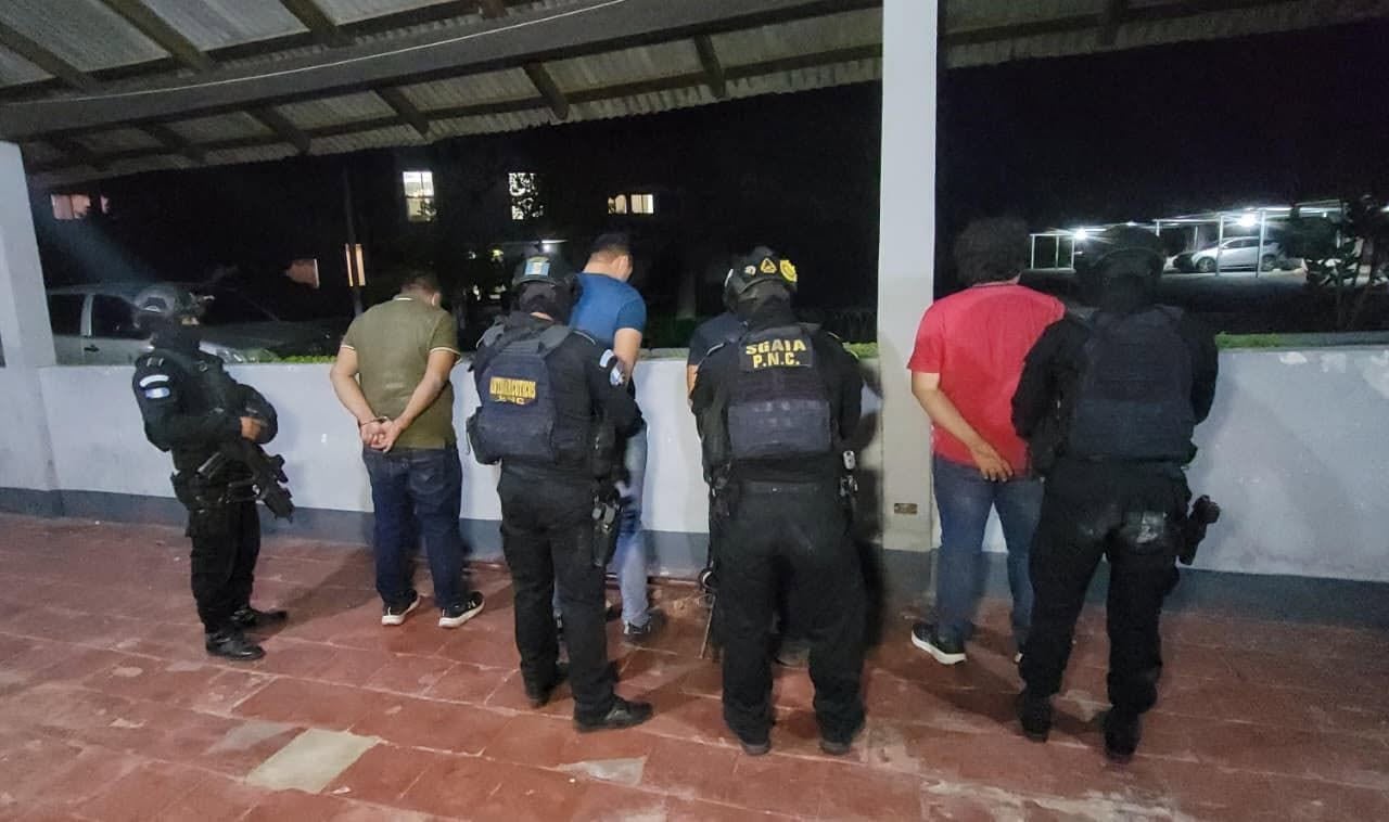 Agentes de la Subdirección General de Análisis de Información Antinarcótica (SGAIA) de la Policía Nacional Civil detienen a varios hombres con las manos inmovilizadas durante un operativo nocturno en un área exterior bajo techo. (PNCdeGuatemala)
