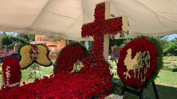 La tumba permanece cubierta por una carpa blanca, rodeada de flores y ornamentos que destacan a simple vista. Crédito: Captura