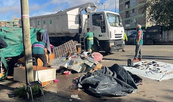 Un camión de basura blanco, personal de Higiene Urbana y policía junto a una lona blanca con múltiples teléfonos celulares y pilas de residuos en la calle