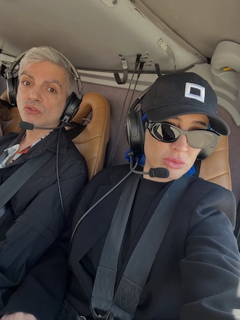 Un hombre y una mujer con gorra y gafas de sol usan auriculares con micrófono dentro de la cabina de una aeronave