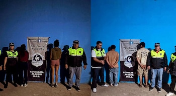 Agentes policiales custodian a cuatro personas colocadas de espaldas frente a carteles de la Policía de Tucumán