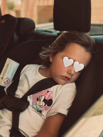 Niña dormida en una silla de coche con el cinturón de seguridad puesto y una camiseta blanca con un dibujo de Minnie Mouse
