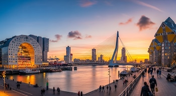 Panorama de Rotterdam al atardecer. Edificio Markthal, puente Erasmus, casas cubo, rascacielos, barcos, grúas portuarias y personas caminando por el muelle.