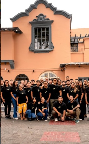 Un grupo de unas 30 personas, vestidas con camisetas negras, posa sonriendo frente al restaurante Fernandini, un edificio de color melocotón con detalles grises