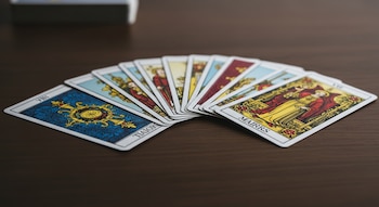 Baraja de tarot tradicional con varias cartas extendidas en abanico sobre una mesa de madera oscura. Las cartas muestran arcanos mayores con figuras.