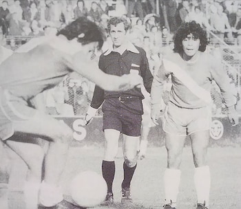 Fotografía en blanco y negro de Diego Maradona y el árbitro Roberto Maino en una cancha junto a un jugador y la pelota