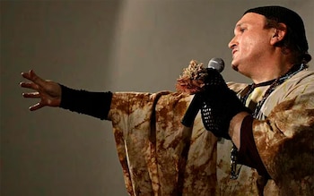 Persona de perfil con gorro oscuro y vestimenta estampada, sosteniendo un micrófono con la mano derecha enguantada y extendiendo la mano izquierda