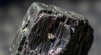 Primer plano de un trozo de carbón mineral con superficie negra y reflejos brillantes.