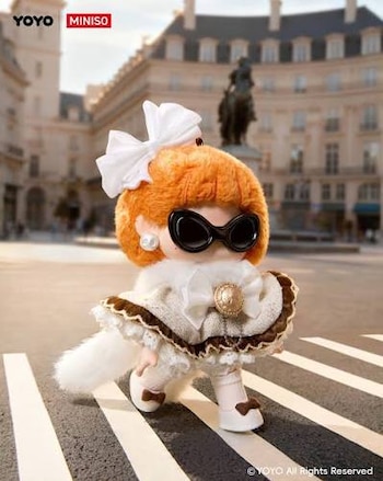 Muñeca de la línea Yo-yo de Miniso con cabello naranja, gafas de sol negras, vestido blanco y zapatos blancos con lazos marrones, en un paso peatonal