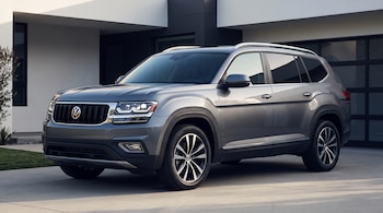 Un automóvil SUV gris metálico de marca Volkswagen estacionado en el camino de entrada de una casa moderna de color blanco y gris.