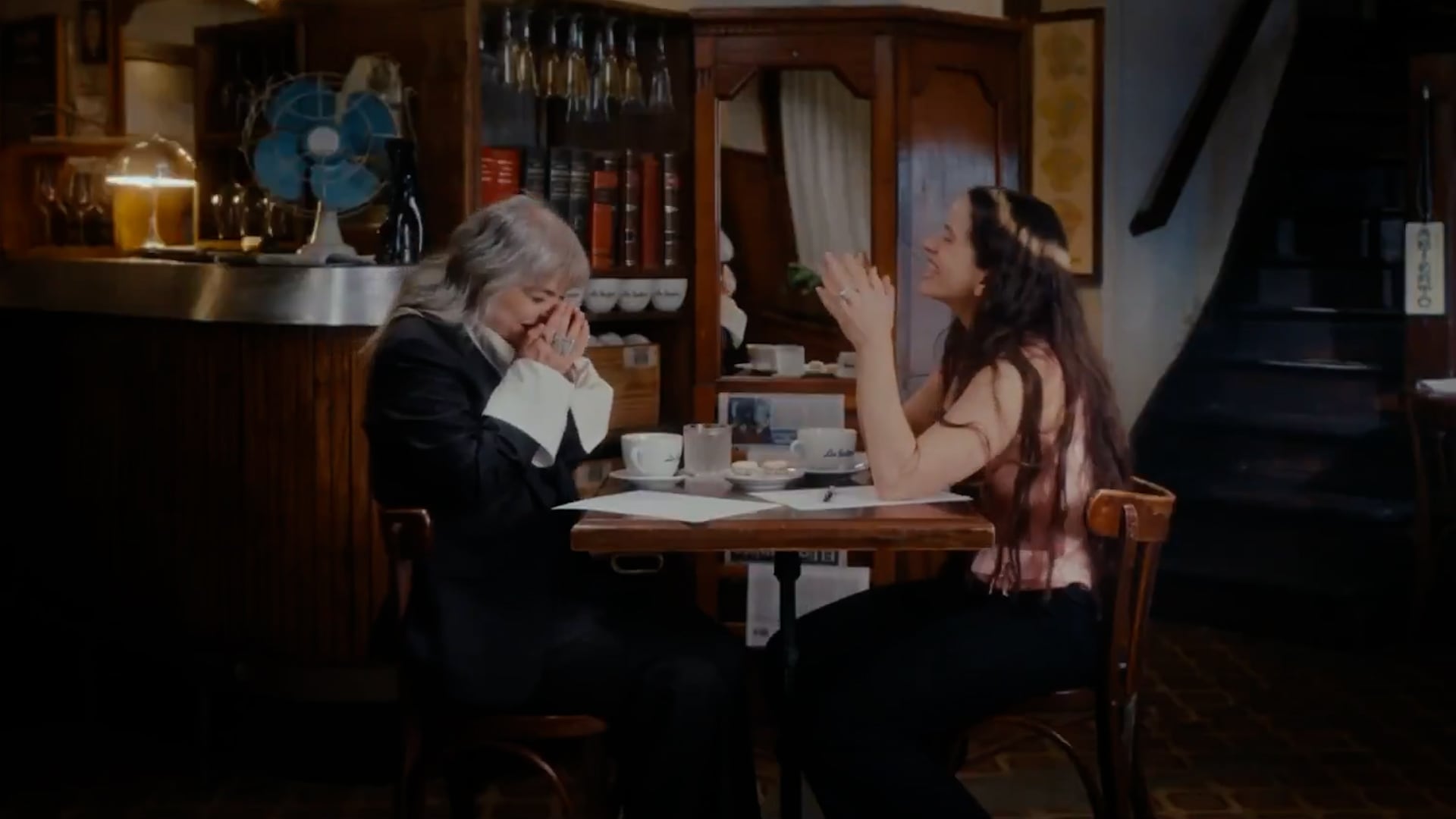 La escritora Mariana Enriquez y la cantante Rosalía comparten un momento de risas y emoción durante su esperada entrevista en un ambiente íntimo de café.