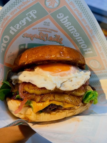 Hamburguesa smash de Angus con bacon, lechuga, tomate, cebolla caramelizada, cheddar y huevo, destacada por su cocción precisa e intensidad de sabores