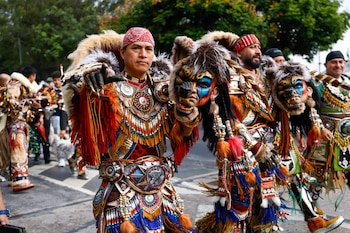 Grupo de personas con trajes tradicionales coloridos, máscaras con rostros pintados, plumas, piel y adornos metálicos