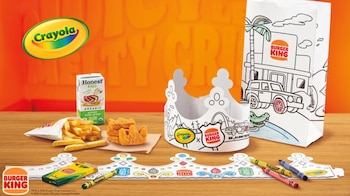 Comida de Burger King para niños con papas fritas, nuggets de pollo, y bebida. Incluye una corona, una bolsa, y crayones Crayola para colorear sobre una mesa de madera y fondo naranja