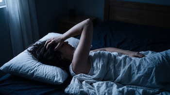 Una mujer está recostada sobre una almohada en una cama con sábanas en una habitación con iluminación tenue