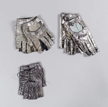 Tres pares de guantes, plateados, sin dedos. Dos pares son brillantes y con cierre de broche. Un par es opaco con cordones. Fondo blanco
