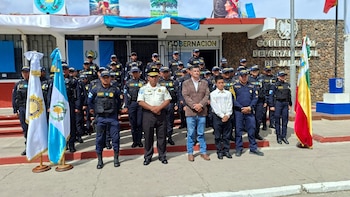 Un grupo de agentes de policía y personas de civil posan alineados frente a un edificio con banderas de Guatemala