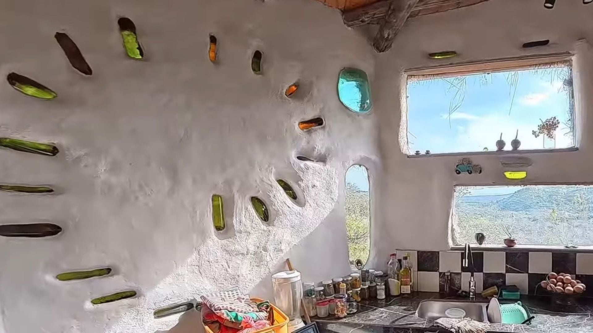 Los muros de barro incorporan doce parabrisas de autos usados y botellas de vidrio para el paso de la luz natural (Yt: @ Crónicas del Cambio)