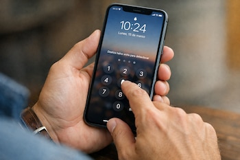 Primer plano de unas manos sosteniendo un smartphone negro con la pantalla de bloqueo encendida, mostrando un teclado numérico y un dedo presionando el número 5.