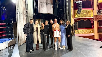 Um grupo de oito pessoas no palco, uma delas vestida de boxeador de sangue. Ao fundo, um ringue de boxe e um camarote de teatro decorado em vermelho e dourado