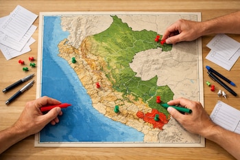 Fotografía cenital de dos manos sobre un mapa físico-político de Perú en una mesa de madera, con pines rojos y verdes marcando regiones y papeles de votación.