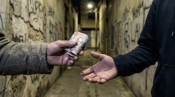 Dos manos intercambian billetes de Costa Rica en un callejón oscuro con paredes grafitadas y luz tenue.