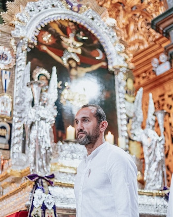 Hernán Barcos con camisa blanca delante del anda ornamentada del Señor de los Milagros con cirios encendidos
