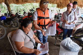La cubana Julia Margarita Bravo Díaz, con chaleco salvavidas, muestra fotos de personas desaparecidas, incluyendo a su hija Meiling Álvarez Bravo y su nieto Samei Armando Reyes Álvarez, a los residentes locales en San José Hueyate, estado de Chiapas, México, el sábado 9 de mayo de 2026 durante una búsqueda de migrantes que desaparecieron a finales de 2024 a lo largo de una ruta marítima de contrabando hacia Estados Unidos. (AP Foto/Edgar H. Clemente)