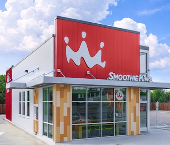 Fachada de un local comercial de Smoothie King con paneles rojos, un logotipo blanco de corona y grandes ventanales de vidrio
