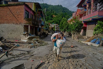 Los residentes transportan sus pertenencias mientras caminan hacia zonas más seguras tras las inundaciones repentinas en Devighat, en el distrito de Nuwakot, Nepal, el jueves 27 de agosto de 2026 (AP/Niranjan Shrestha)
