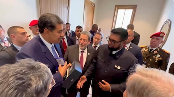 Nicolás Maduro, en traje azul, y el presidente de Guyana, Irfaan Alí, en traje oscuro, se dan la mano en una sala llena de personas. Hay un hombre con boina roja al fondo