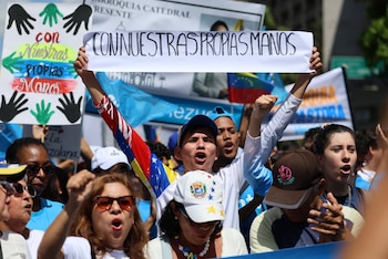 Multitud de manifestantes al aire libre, con la bandera de Venezuela, algunos con puños en alto. Un joven sostiene un cartel con 'CON NUESTRAS PROPIAS MANOS'