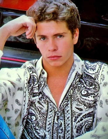 Retrato de un joven con camisa de estampado cachemira en blanco y negro, apoyando una mano sobre su cabeza