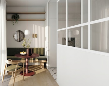 Un rincón de comedor moderno con un banco verde oscuro, mesa redonda de color rojizo, sillas de madera, y plantas colgantes junto a una ventana con cortinas claras.