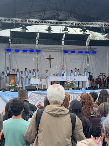 Sacerdotes con vestimentas religiosas celebran una ceremonia sobre un escenario frente a una multitud vista de espaldas