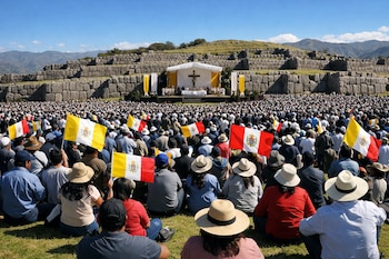 Gran multitud de personas sentadas en el pasto con banderas de Perú y del Vaticano, viendo un altar con una cruz al aire libre y muros de piedra.