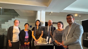 Seis personas, tres mujeres y tres hombres, posan sonrientes en una sala con una vitrina transparente que contiene un espécimen de roca
