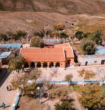 Vista aérea de un edificio con arcadas y tejado naranja junto a una plaza con árboles frente a cerros áridos