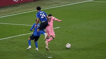 Tres jugadores de fútbol. Dos con uniforme azul, uno con el número 24 y otro con el nombre parcialmente visible. Un jugador con uniforme rosa y el número 10. Un balón de fútbol en el césped verde.