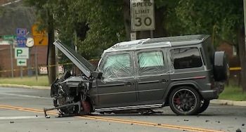 Una camioneta gris con el frente destruido y el capó levantado sobre una calle junto a señales de tránsito