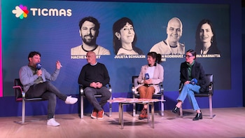 Cuatro personas sentadas en sillas negras sobre un escenario de madera. Detrás, una pantalla azul muestra el logo de Ticmas y retratos de los oradores