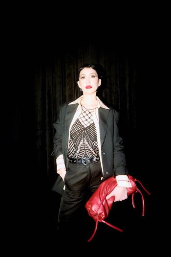 Sofía Gala viste un saco negro, un top tejida calado, un pantalón oscuro y un bolso rojo sobre un fondo negro