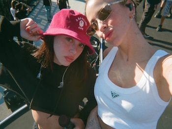 Primer plano de dos mujeres tomando una selfie; una lleva un sombrero de pescador rosa y la otra gafas de sol y una camiseta blanca