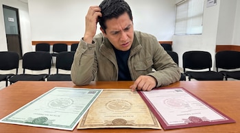 Un hombre se rasca la cabeza mientras mira tres actas de nacimiento mexicanas en colores verde, sepia y rojo sobre un escritorio de madera.