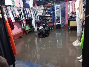 Interior de un local inundado con agua turbia cubriendo el piso. Se ven estantes con ropa, una motocicleta negra, un espejo y maniquíes con ropa
