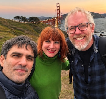 Tres personas sonríen a la cámara al aire libre con el puente Golden Gate de San Francisco y el atardecer de fondo