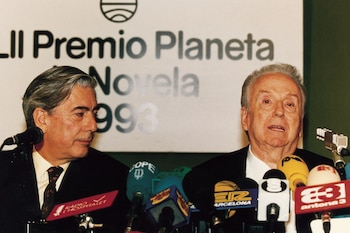 Dos hombres en traje se encuentran detrás de una mesa con micrófonos ante un panel del Premio Planeta de Novela de 1993
