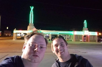 Dos hombres se toman una fotografía de noche en una calle con un edificio iluminado con neón verde al fondo